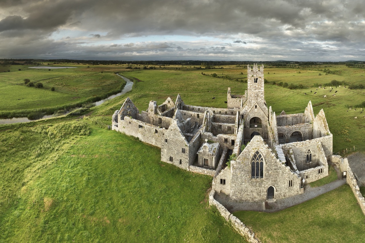 Luftbild der Klosterruine Ross Abbey inmitten grüner Wiesen unter dunklen Wolken