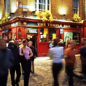 Abendliche Straßenszene vor der roten Fassade des Pubs The Temple Bar in Dublin, Passanten teils in Bewegungsunschärfe